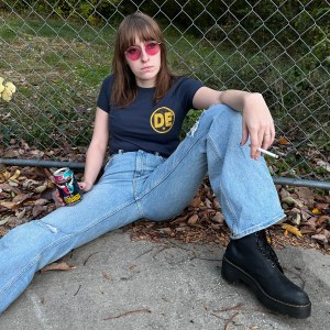 Girl sitting on the ground outdoors wearing the Romanian Girl t-shirt in black