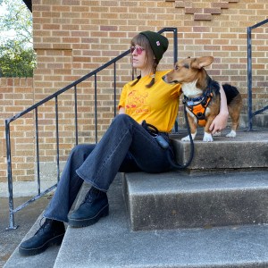 A girl wearing a yellow Dog Walker t-shirt sitting on cement steps with her dog